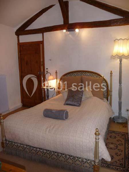 Chambre avec un lit double, lampe sur table de chevet, parquet, tapis et poutres apparentes au plafond.