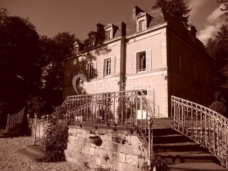 Manoir ancien en pierre avec balustrades en fer forgé, entouré d'arbres, capturé dans une teinte sépia.