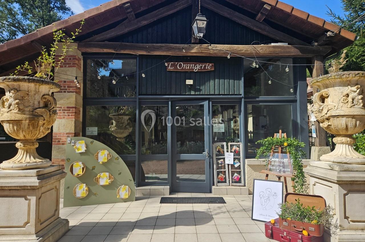Façade d'un bâtiment nommé ’L'Orangerie’ avec des décorations, des plantes et une valise devant l'entrée.