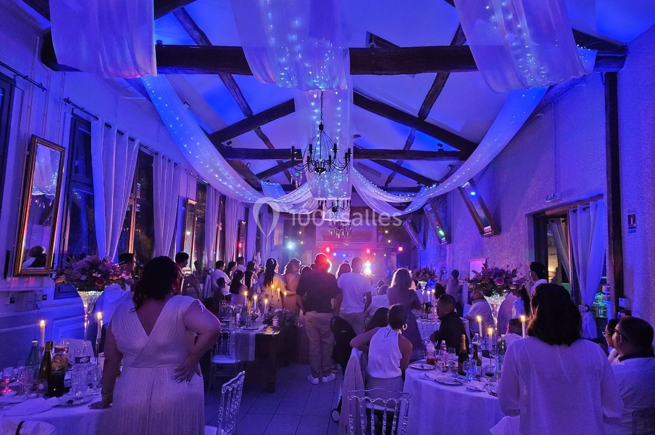 Salle de réception décorée avec des guirlandes lumineuses, des invités assis et debout lors d'une soirée festive.