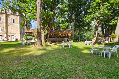Deux fauteuils en rotin décorés, placés sous une arche ornée de fleurs et de tissus, dans un jardin verdoyant.