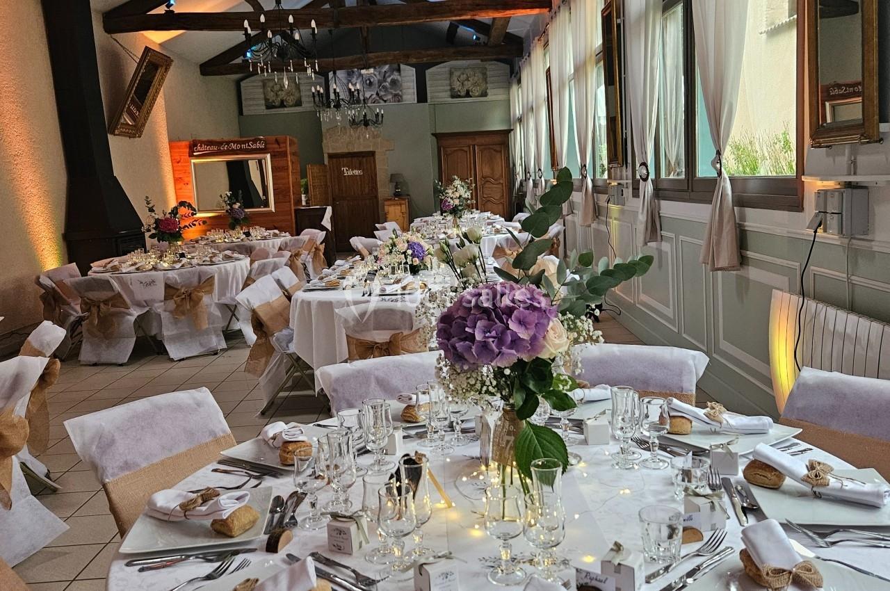 Salle de réception décorée avec des tables rondes élégamment dressées, ornées de fleurs et éclairées par une lumière…