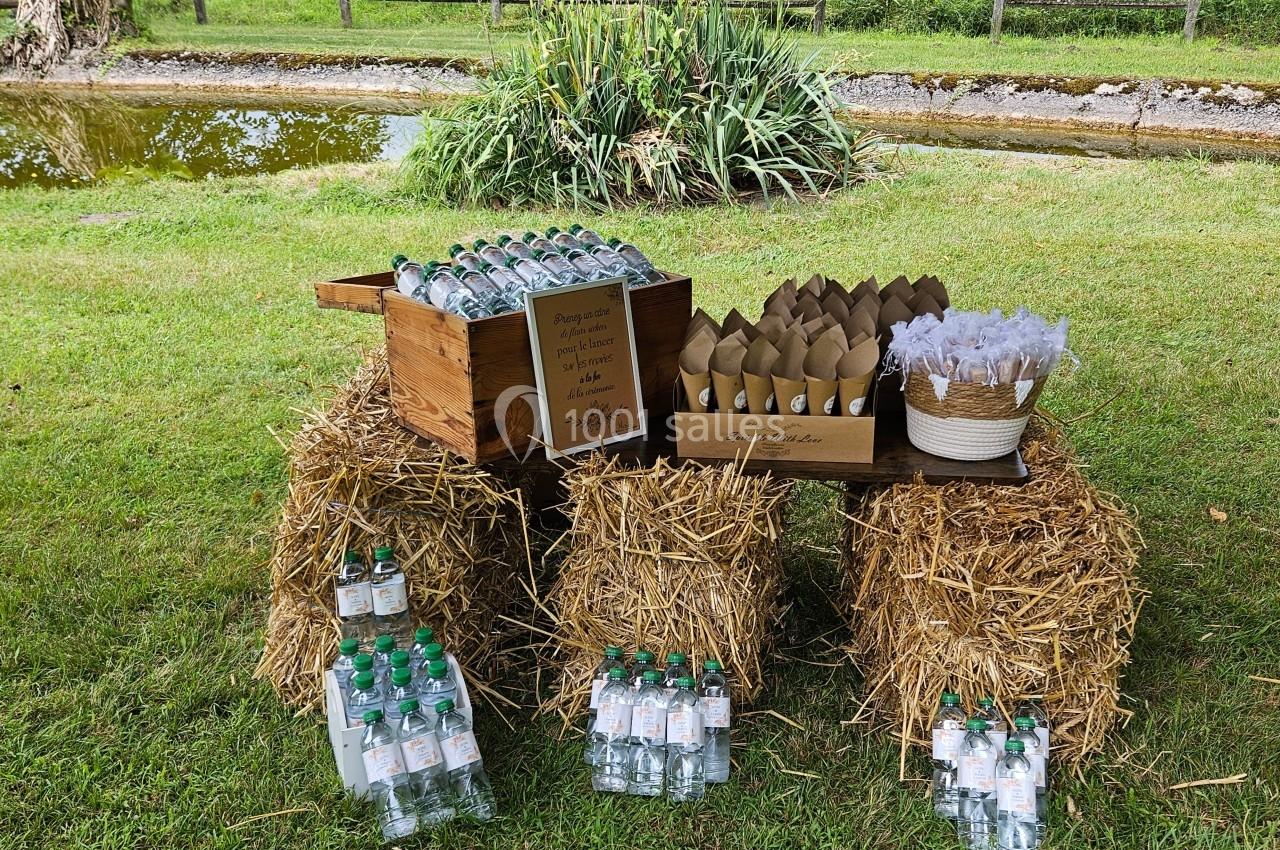 Bouteilles d'eau et cônes en papier disposés sur des bottes de paille dans un cadre champêtre près d'un étang.