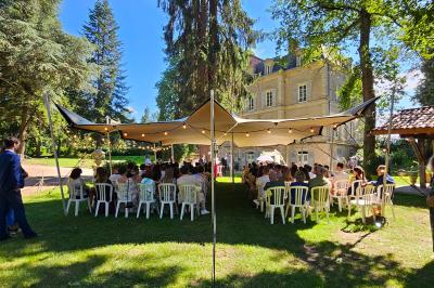 Deux fauteuils en rotin décorés, placés sous une arche ornée de fleurs et de tissus, dans un jardin verdoyant.