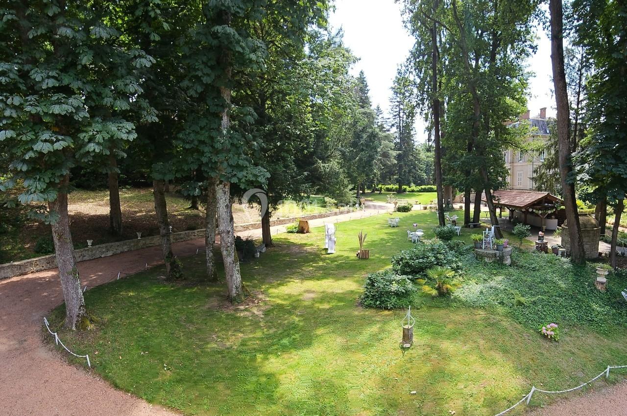 Jardin verdoyant avec pelouse, arbres, allée en gravier et quelques bancs près d'un bâtiment en arrière-plan.