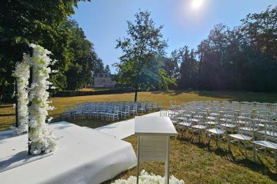 Deux fauteuils en rotin décorés, placés sous une arche ornée de fleurs et de tissus, dans un jardin verdoyant.