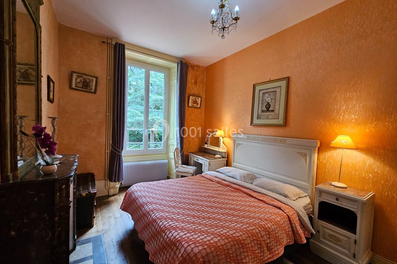 Chambre avec lit double, murs orange, mobilier classique, cheminée, et fenêtre donnant sur des arbres.