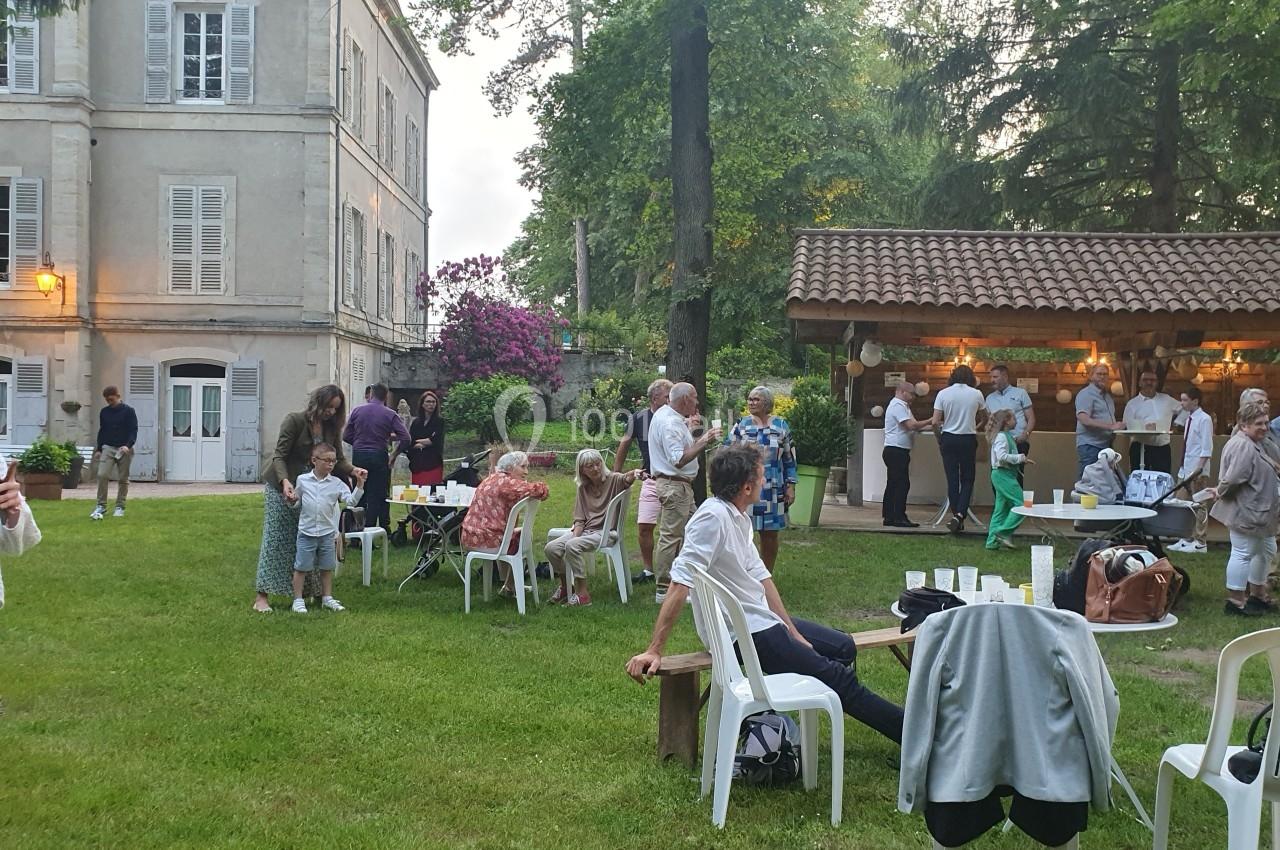 Groupe de personnes rassemblées dans un jardin, près d'un bâtiment ancien et d'un espace couvert avec un bar.