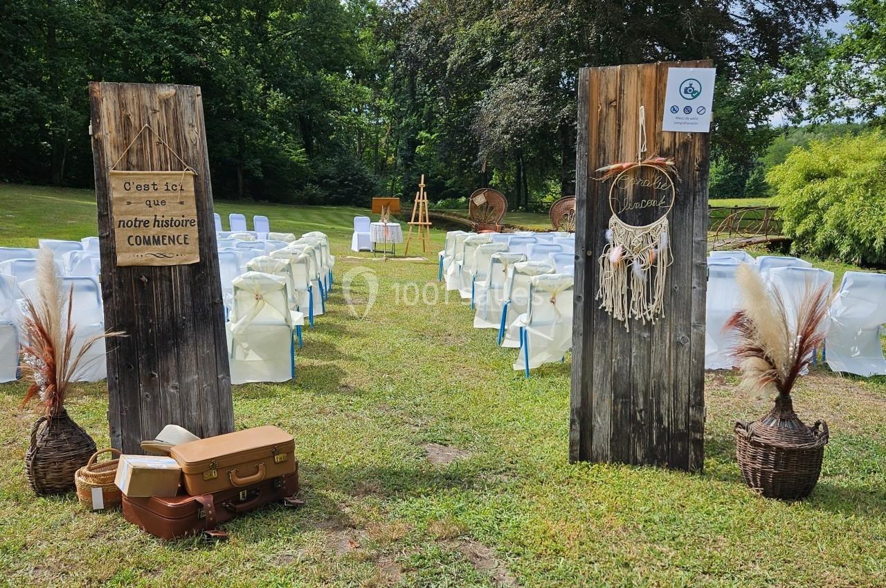 Allée centrale d'une cérémonie en plein air avec des chaises alignées, des panneaux en bois et des décorations bohèmes.