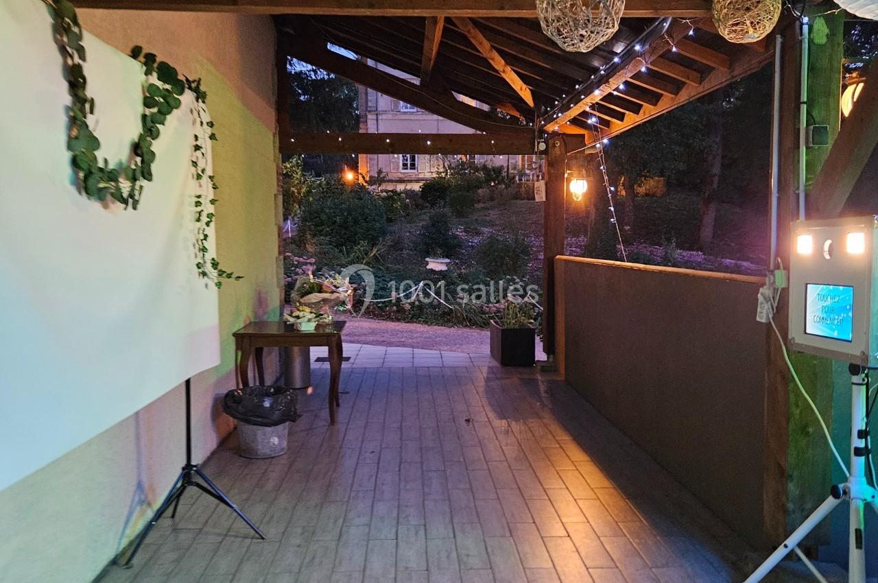 Passage couvert décoré de lanternes suspendues, guirlandes végétales et éclairages doux, donnant sur un jardin.