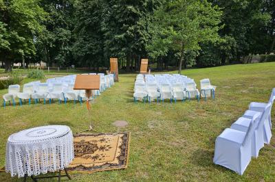 Deux fauteuils en rotin décorés, placés sous une arche ornée de fleurs et de tissus, dans un jardin verdoyant.