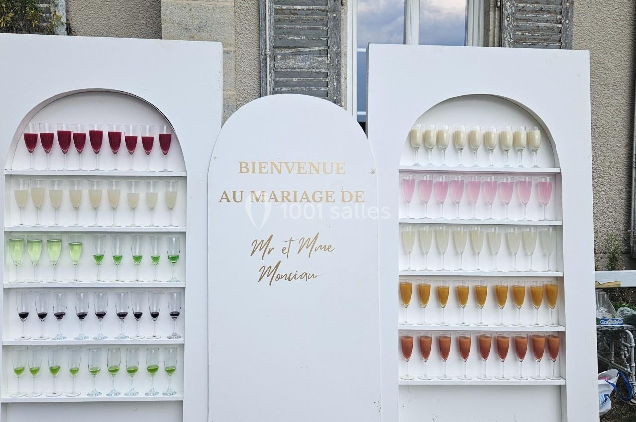Mur décoratif avec des rangées de coupes de champagne colorées, installé devant un bâtiment en pierre.