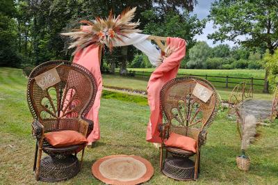 Deux fauteuils en rotin décorés, placés sous une arche ornée de fleurs et de tissus, dans un jardin verdoyant.