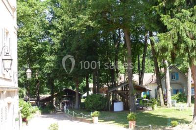 Espace couvert avec canapé, tables et chaises en bois, entouré de verdure visible à travers les ouvertures.