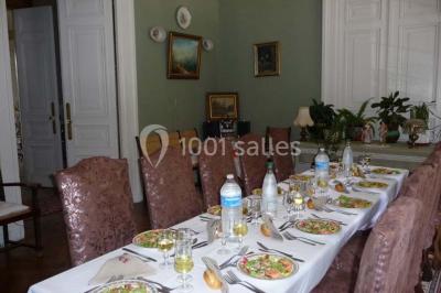 Espace couvert avec canapé, tables et chaises en bois, entouré de verdure visible à travers les ouvertures.