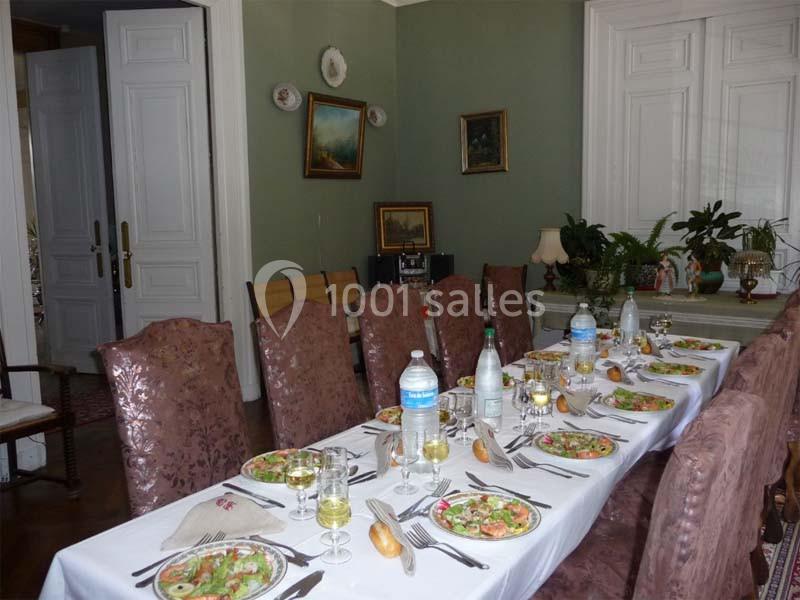Table dressée pour un repas, avec assiettes de salade, couverts, verres, bouteilles d'eau et décor intérieur classique.
