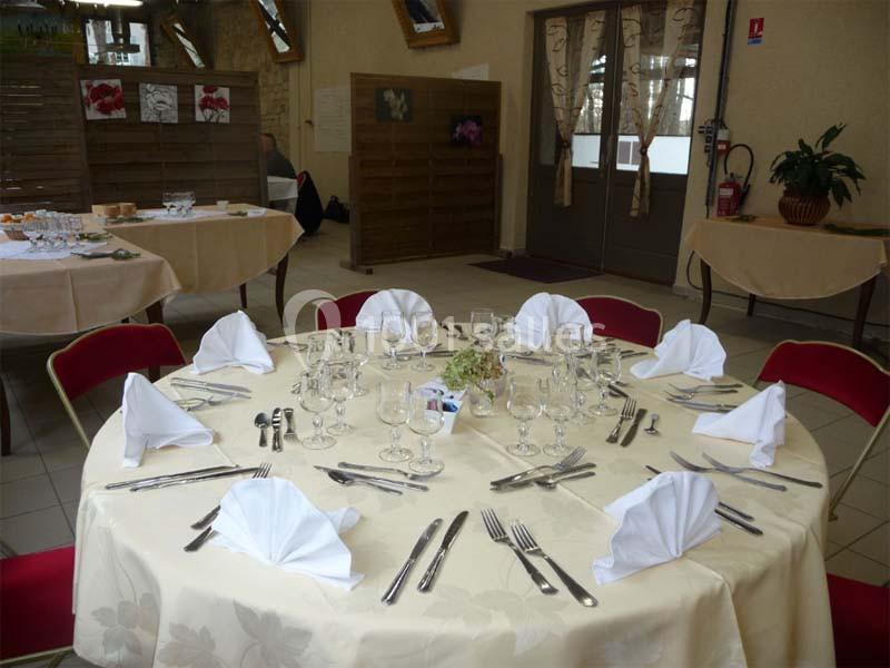 Table ronde dressée avec nappes et serviettes pliées, entourée de chaises rouges, dans une salle de réception lumineuse.