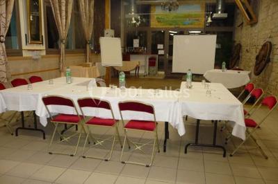 Espace couvert avec canapé, tables et chaises en bois, entouré de verdure visible à travers les ouvertures.