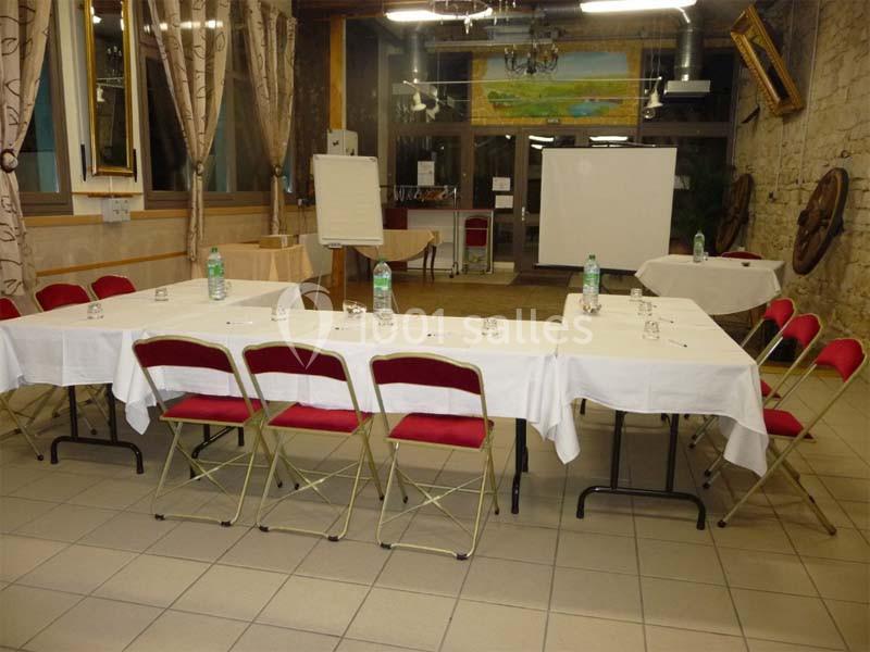 Salle de réunion avec tables disposées en U, nappées de blanc, chaises rouges et matériel de présentation.