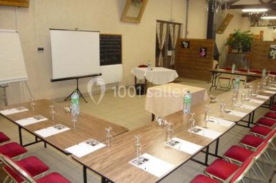 Espace couvert avec canapé, tables et chaises en bois, entouré de verdure visible à travers les ouvertures.