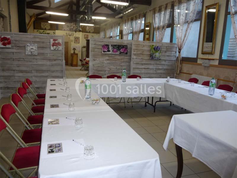 Salle aménagée avec des tables en U, nappées de blanc, chaises rouges et décorations murales florales.