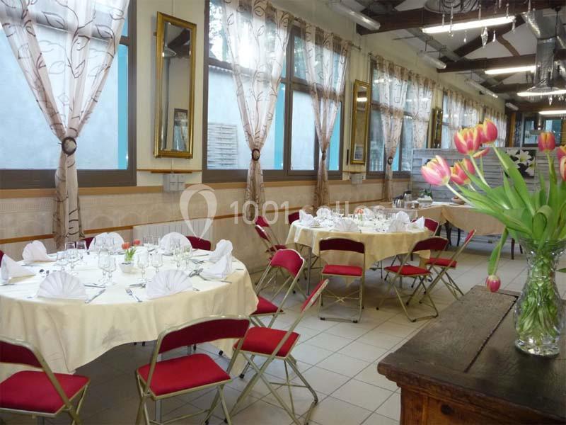 Salle de réception lumineuse avec tables rondes dressées, chaises rouges et vase de tulipes au premier plan.
