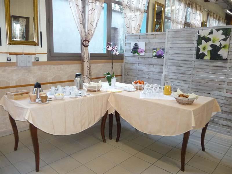 Tables dressées avec boissons chaudes, jus de fruits, viennoiseries et vaisselle dans une salle lumineuse.