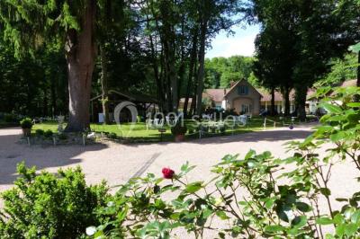 Espace couvert avec canapé, tables et chaises en bois, entouré de verdure visible à travers les ouvertures.