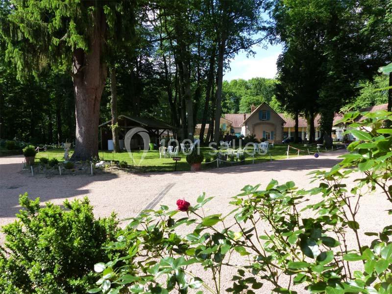 Jardin verdoyant avec des chaises blanches, une maison en arrière-plan et des arbres entourant l'espace.