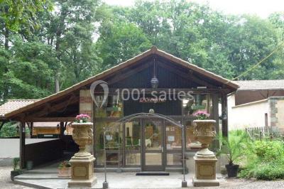 Espace couvert avec canapé, tables et chaises en bois, entouré de verdure visible à travers les ouvertures.
