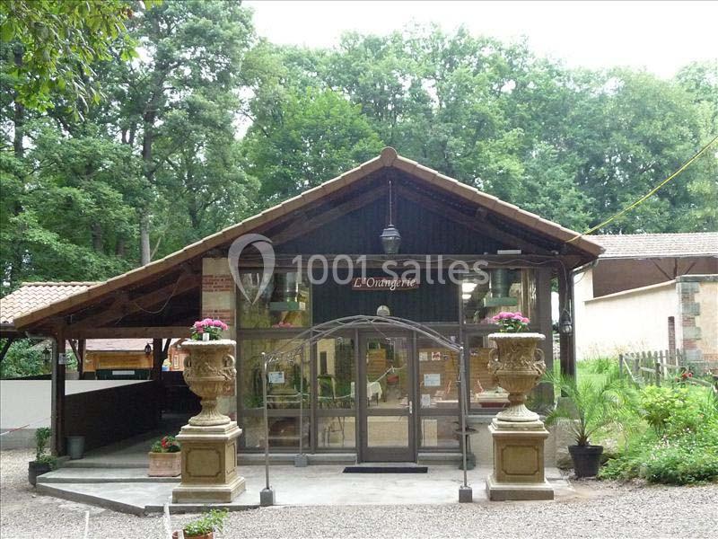 Façade d'un bâtiment en bois avec une entrée vitrée, entouré de végétation et décoré de grandes jardinières.