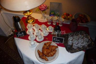 Espace couvert avec canapé, tables et chaises en bois, entouré de verdure visible à travers les ouvertures.