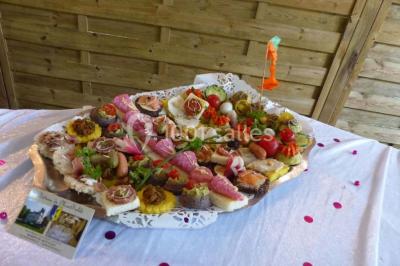 Espace couvert avec canapé, tables et chaises en bois, entouré de verdure visible à travers les ouvertures.