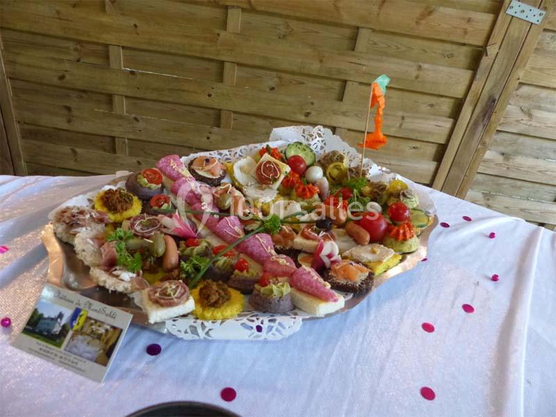 Plateau de canapés variés avec légumes, charcuterie et décorations, posé sur une nappe blanche parsemée de confettis roses.