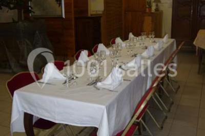 Espace couvert avec canapé, tables et chaises en bois, entouré de verdure visible à travers les ouvertures.