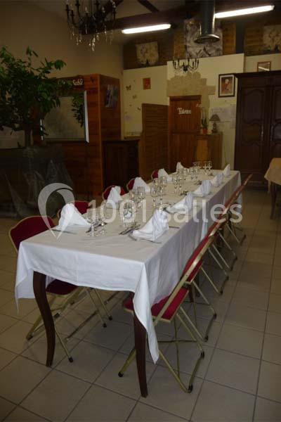 Table dressée avec nappes blanches, serviettes pliées et verres, entourée de chaises dans une salle décorée simplement.