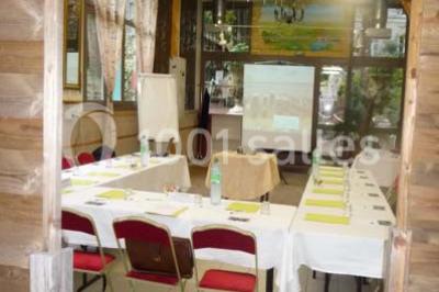 Espace couvert avec canapé, tables et chaises en bois, entouré de verdure visible à travers les ouvertures.