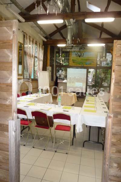 Salle de réunion avec tables disposées en U, chaises rouges, écran de projection et décorations rustiques.