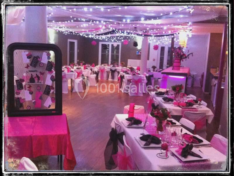 Salle de réception décorée avec des tables dressées, des nappes roses et blanches, et un éclairage festif.