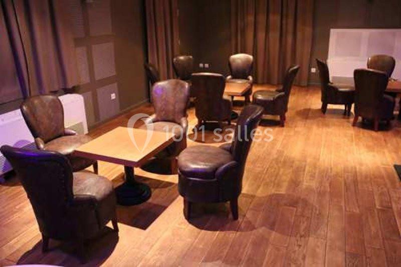 Salle avec parquet en bois, tables carrées et fauteuils en cuir marron disposés dans un espace sobre et chaleureux.