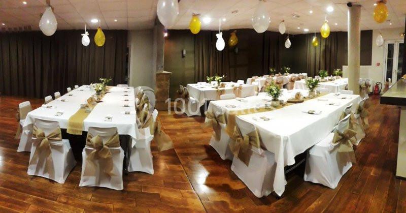 Salle de réception avec tables décorées de nappes blanches, chemins de table beige et chaises ornées de nœuds.