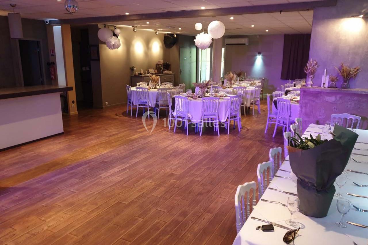 Salle de réception décorée avec des tables dressées, des chaises blanches et des éléments décoratifs suspendus.