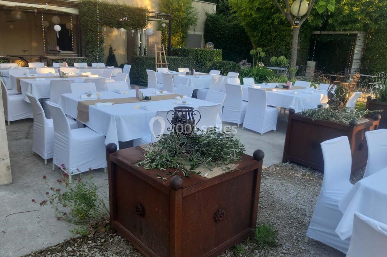Tables et chaises blanches disposées en extérieur pour un événement, entourées de verdure et de décorations simples.