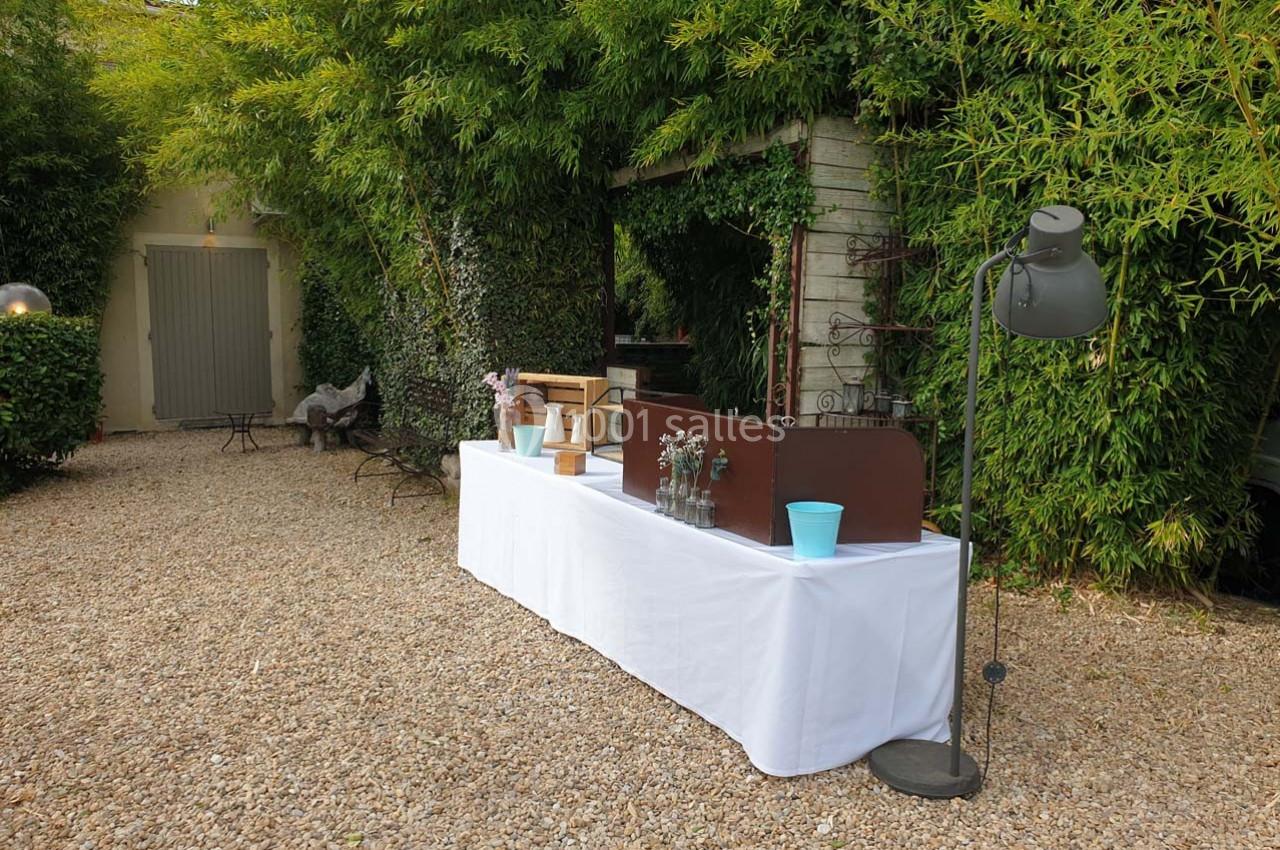 Table dressée avec nappe blanche sur un sol gravillonné, entourée de végétation et d'une lampe sur pied.