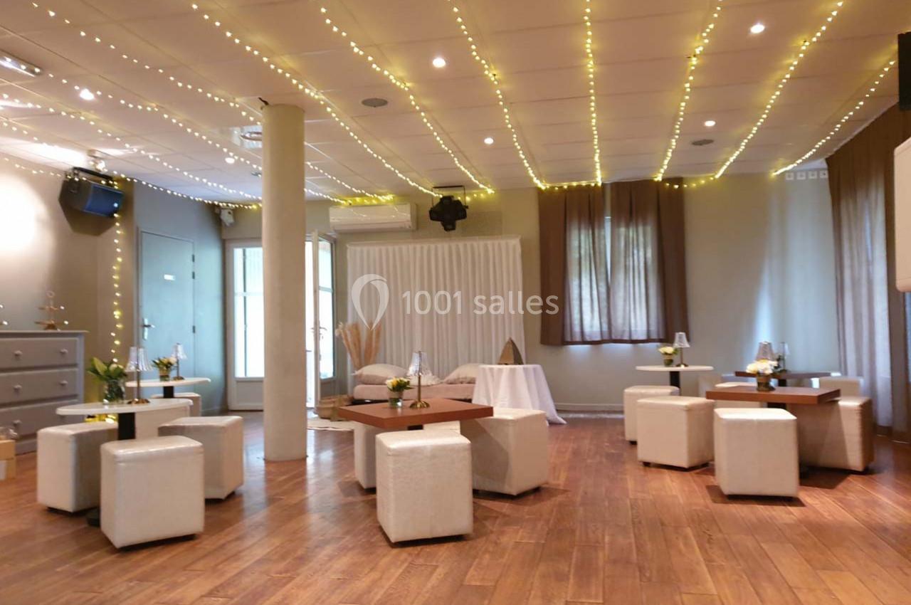 Salle lumineuse avec parquet, décorée de guirlandes lumineuses, tables basses en bois et poufs blancs.