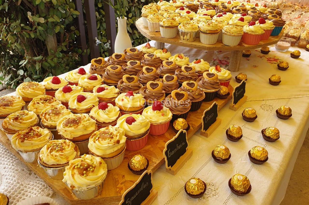 Plateau de cupcakes variés décorés de crème, fruits et chocolat, disposés sur une table avec des ferreros en accompagnement.