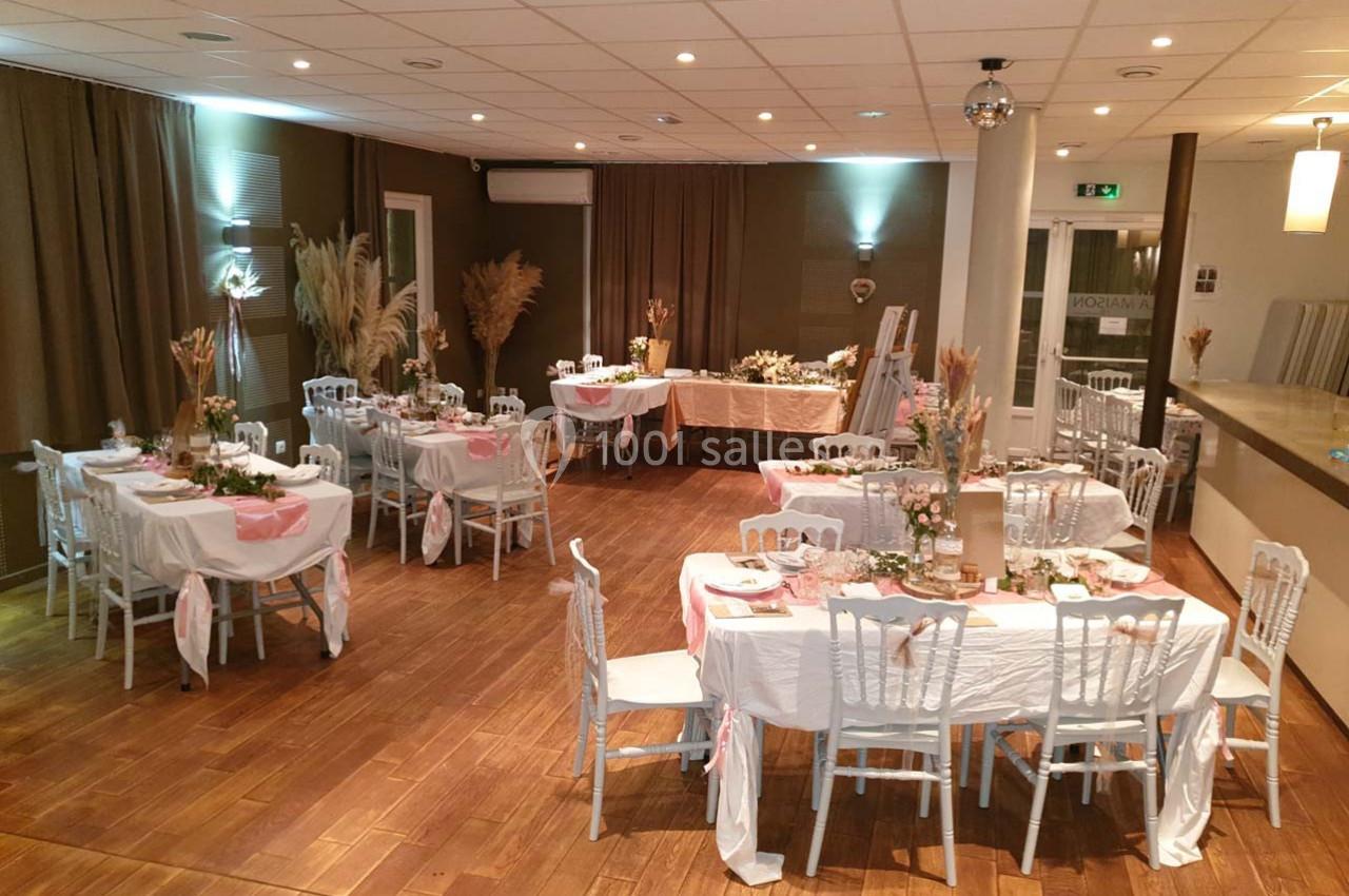 Salle de réception décorée avec des tables dressées, nappes blanches, chaises assorties et ornements végétaux.