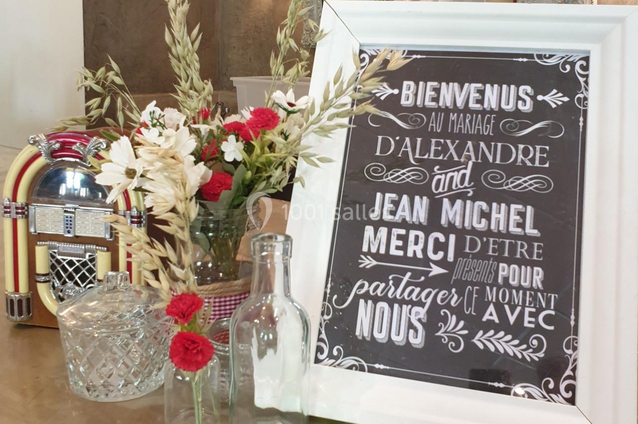 Panneau de bienvenue pour un mariage, entouré de fleurs, d'un jukebox et de carafes en verre sur une table.