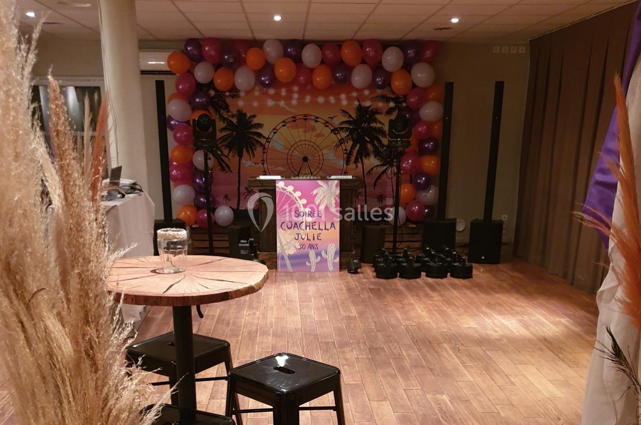 Décoration intérieure avec ballons colorés, table haute et fond thématique Coachella, dans une salle éclairée.