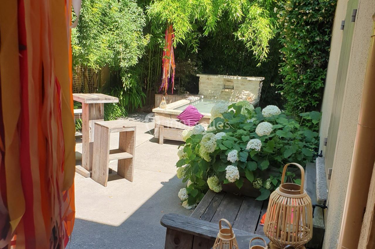 Terrasse ensoleillée avec mobilier en bois, hortensias en fleurs, bambous en arrière-plan et lanternes décoratives.